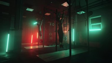 Spor salonundaki iki adam ve bir kadın karanlık neon ışıkta birlikte barfiks çekiyorlar. Fitness ve eğitim atmosferi