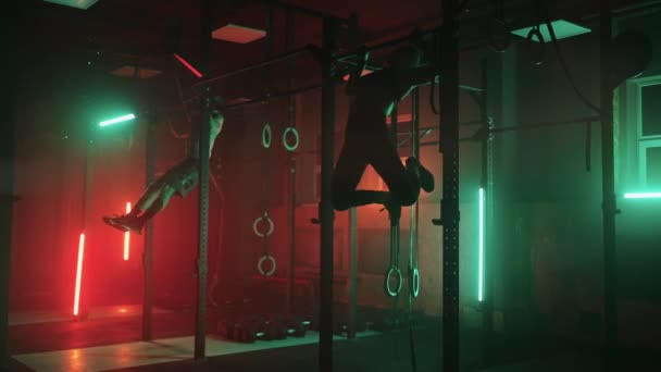 Dwóch mężczyzn i kobieta na sali gimnastycznej podciągają się razem w ciemnym neonowym świetle. Atmosfera sprawności i treningu — Wideo stockowe