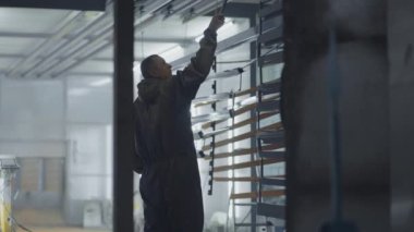 Kamera çalışan adamı takip ediyor fırından boya pişirmek için parça çıkarıyor. Çelik metal ürünleri üretimi için fabrika. Boyama atölyesi