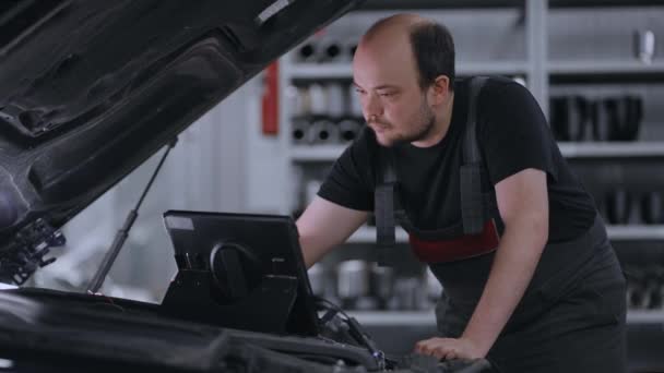 Meccanico maschile utilizza un computer tablet con un software di diagnostica della realtà aumentata. Specialista Ispezione della vettura al fine di trovare componenti rotti all'interno del vano motore. Servizio auto moderno. — Video Stock