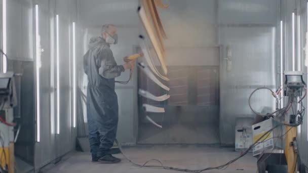 Ein Mann in Schutzanzug und Maskenmaler sprüht Farbe auf die Teile. Kleinunternehmen Malerei-Geschäft. Werkstatt zum Lackieren von Teilen. — Stockvideo