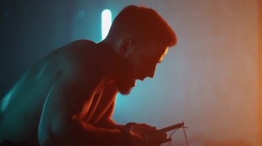 Yorgun sporcu karanlık jimnastik salonunda, spor egzersizleri arasında dinleniyor, zor nefes alıyor.