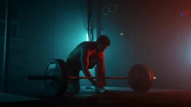 Güçlü atlet karanlık spor salonunda halteri kaldırmaya hazırlanıyor. Profesyonel sporcu salonda antrenman yapıyor.