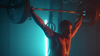 Genç halterci spor salonunda halterle antrenman yapıyor, ağırlık kaldırıyor ve yere düşüyor.