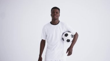 Beyaz arka plandaki Afro-Amerikan futbolcunun portresi. Genç sporcu topu tutuyor.