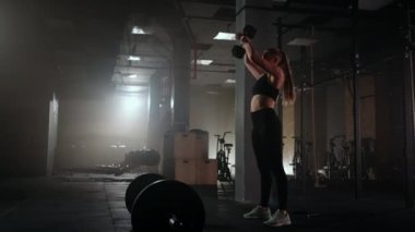 Jimnastik salonunda genç bir kadının güç eğitimi, bayan spor salonunda dambılları kaldırıyor.