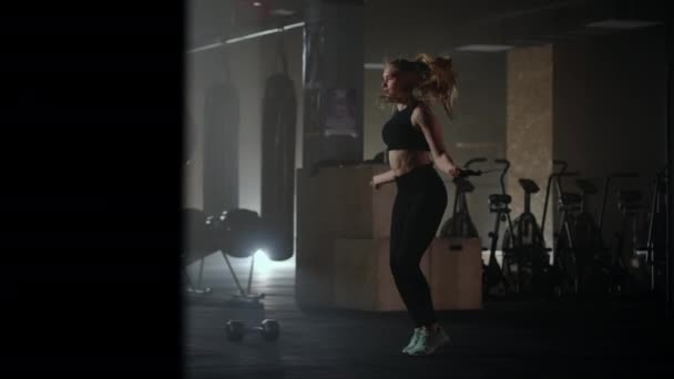 Joven mujer deportiva está saltando la cuerda, saltando y calentando el cuerpo en el gimnasio antes del entrenamiento — Vídeo de stock