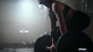 Sarışın sporcu kadın spor salonunda sıkı çalışıyor, halteri kaldırıyor, spor salonunda ağır çekimde çalışıyor.