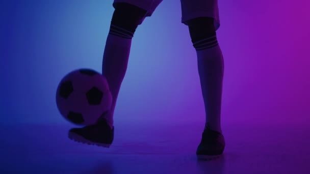 Pemain sepak bola bermain dengan bola keepie-uppie di studio dengan warna biru dan ungu, closeup kaki — Stok Video