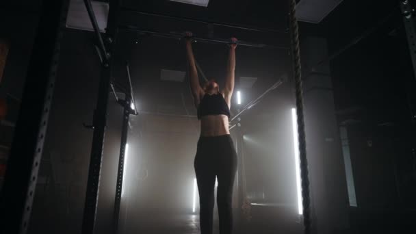 Sportos nő húzza fel a keresztrudat a tornateremben, egyedül edz a sötét fitneszteremben éjszaka. — Stock videók