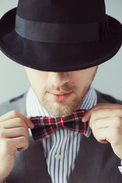 Portrait of a man in the black hat correcting his bow-tie — Stock Photo, Image