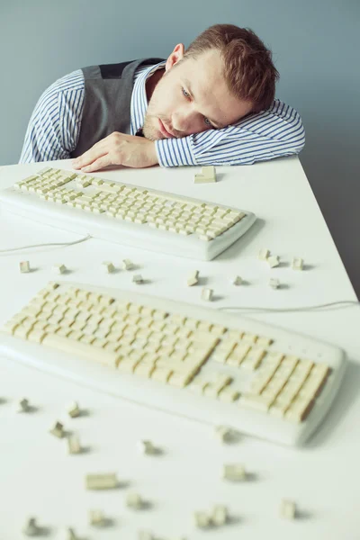 Giovane sdraiato sul tavolo con tastiere per computer — Foto Stock