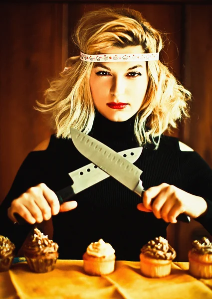 Femme au foyer blonde et cupcakes avec des couteaux — Photo