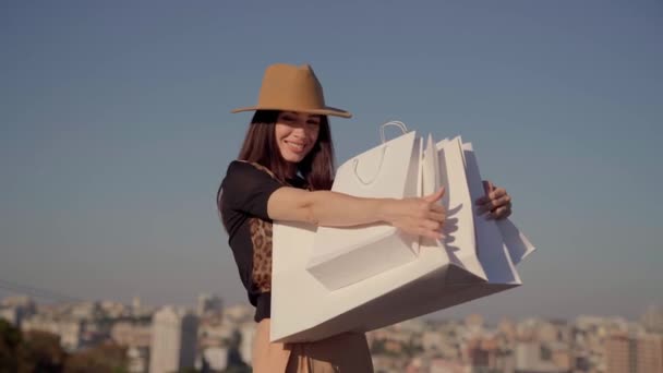 Chica de moda sostiene bolsas de compras contra el cielo azul — Vídeos de Stock