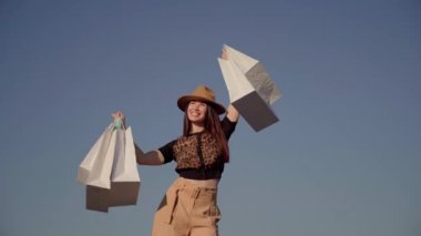 Alışveriş meraklısı genç bir kadın dışarıda alışveriş torbalarıyla dans ediyor.