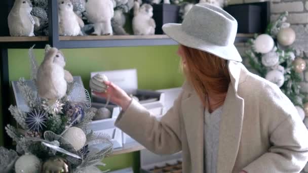 Mujer joven en sombrero de elegir la decoración de Navidad en la tienda — Vídeo de stock