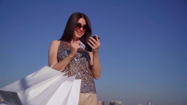 Menina fazendo compras on-line segurando cartão de crédito e telefone — Vídeo de Stock