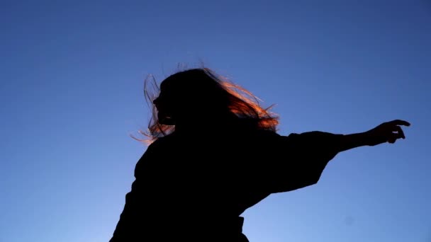 Silhueta de menina dançando no vestido contra o céu ao pôr do sol — Vídeo de Stock