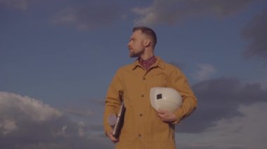 Construction industry worker holds helmet, plans and laptop