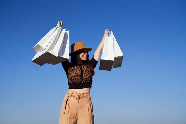 Menina morena bonito no chapéu levantando sacos de compras ao ar livre — Fotografia de Stock
