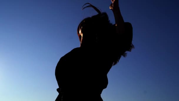 Танцующая девушка силуэт против голубого неба на закате — стоковое видео
