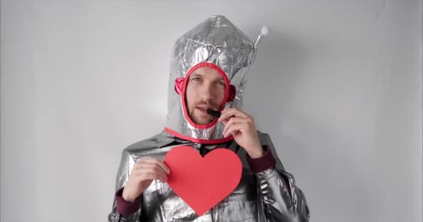 Симпатичный мужчина в костюме космонавта с красной бумагой в форме сердца — стоковое видео