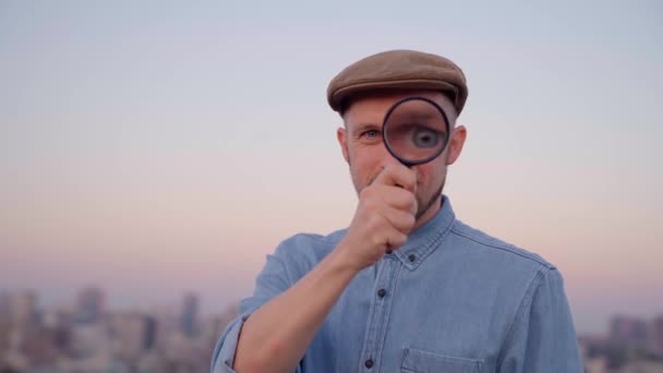 Мужчина с увеличительным стеклом на открытом воздухе с видом на город — стоковое видео