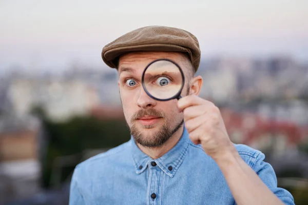 Man looking using magnifying glass outdoor with urban view — Stock Photo, Image