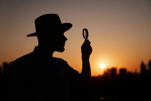 Siluet erkek gün batımında büyüteç kullanıyor.