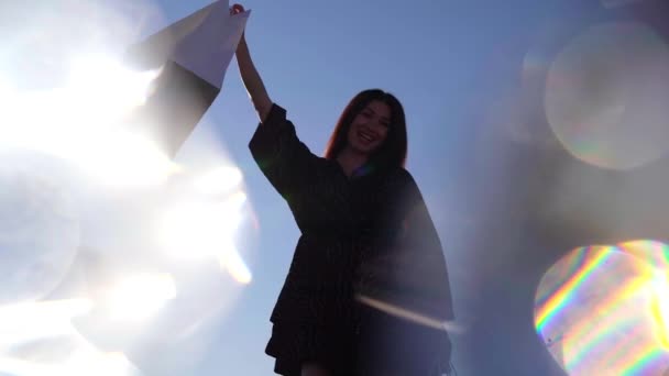 Chica mostrando bolsas de compras contra el cielo y el sol-destellos efecto — Vídeos de Stock