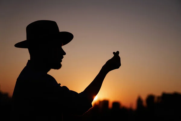 Silueta masculina en sombrero mostrando el corazón coreano al atardecer — Foto de Stock