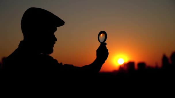 Detetive silhueta masculina ao pôr do sol usando lupa — Vídeo de Stock