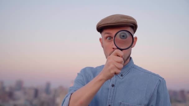 Schattig mannetje maken groot oog met vergrootglas met stedelijk uitzicht — Stockvideo