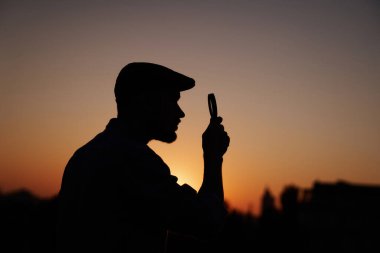 Gün batımında siluet erkek dedektif büyüteç kullanıyor.