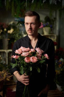 Siyah gömlekli şık maço adam pembe gül buketi tutuyor.