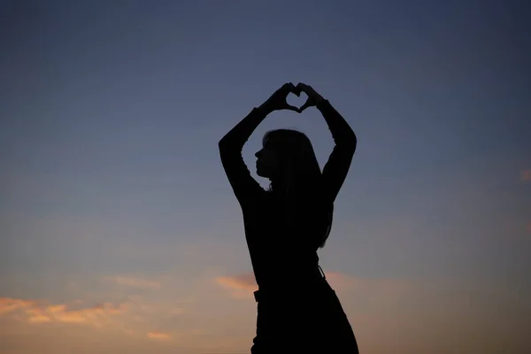 Silueta de niña haciendo corazón o símbolo de amor al atardecer — Foto de Stock