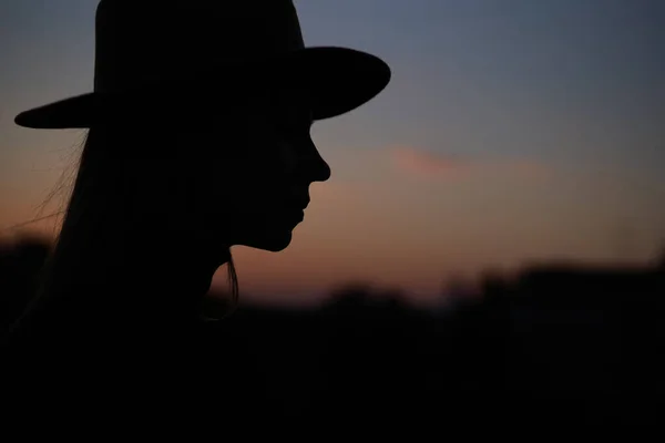 Gün batımında şapkalı, şık, uzun saçlı bir kadın silueti. Stok Fotoğraf
