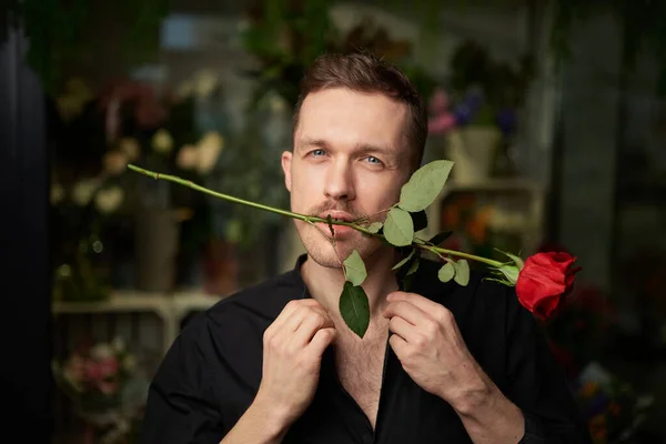 Cheerful macho man in black shirt with red rose in his mouth — Stock Photo, Image