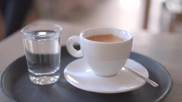 Fehér csésze kávé az asztalon egy pohár vízzel, 4k videó — Stock videók