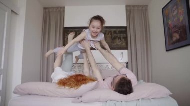 Happy family together on a bed lying having fun together. Funny weekend concept. Mother, father and daughter making plane with kid. High quality 4k video footage