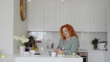 Videoconference call or online education concept. Female having video conversation saying hello with hands. Woman having online video chat or meeting at the kitchen at home. High quality 4k footage
