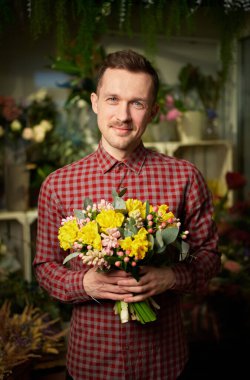 Theme of love, dating or romance concept. Attractive male in shirt holding beautiful bouquet of yellow and pink fresh flowers. Mothers Day, Valentines Day or International Women Day holiday