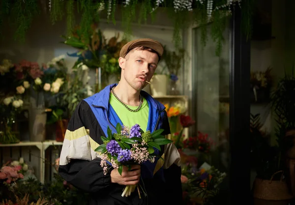 Congratulating with flowers: portrait of man in peaked cap and tracksuit holding spring flower bouquet standing indoor in flower store. Love, dating or romance concept. High quality photo