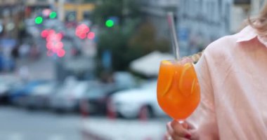 Aperol spritz cocktail, close up shot. Girl holds in hand glass of Spritz in bar with evening city urban background. Refreshing alcoholic drink in the hands of a girl. High quality 4k footage