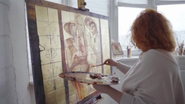 Artwork creative painting. Talented female painter drawing with paintbrush at canvas in studio workshop interior. Young woman artist painting picture on canvas in art studio. High quality 4k footage
