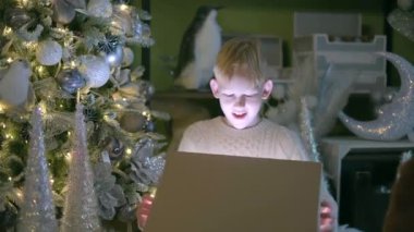 Happy small boy opens New Year or Christmas 2023 gift and get surprised emotion. Joyful and cheerful caucasian kid near the Xmas tree with gift. High quality 4k footage