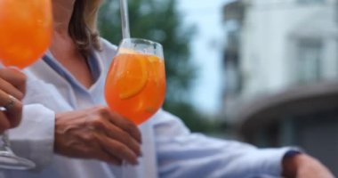 Friends hanging out in a bar clinking with glasses of Spritz cocktail. Aperol spritz cocktail, close up shot. Refreshing alcoholic drink in the hands. No faces. High quality 4k footage