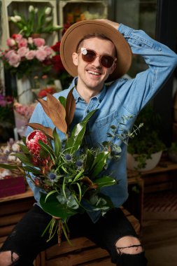 Mothers Day, Valentines Day or International Womens Day concept. Hipster male person in sunglasses and hat with fresh spring flower bouquet in flower shop. High quality image