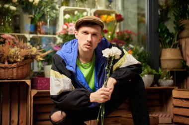 Zirvedeki şapkalı ve eşofmanlı kürdanlı erkek holiganın portresi. Çiçekçide bahar karanfili buketi tutuyor. Aşk, flört ya da romantizm kavramı. Yüksek kalite fotoğraf