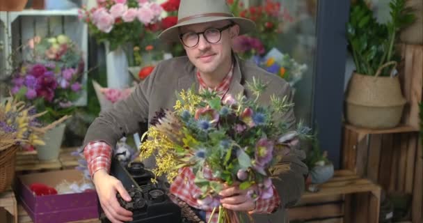 Atrakcyjny Mężczyzna Starą Maszyną Pisania Okularach Kapeluszu Trzymający Bukiet Kwiatów — Wideo stockowe